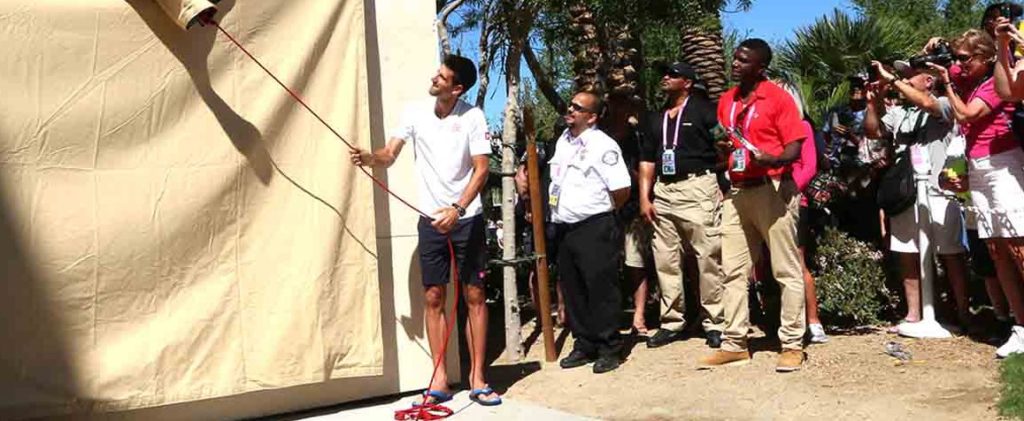 Novak Djokovic pulls the drape to his mural before the crowd and media
