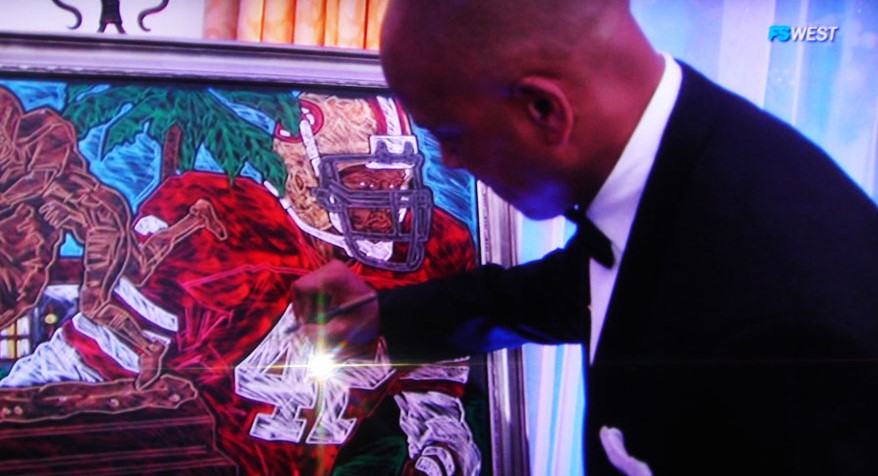 Hall of Famer Ronnie Lott signs a canvas giclee painting of the Lott Trophy Mural